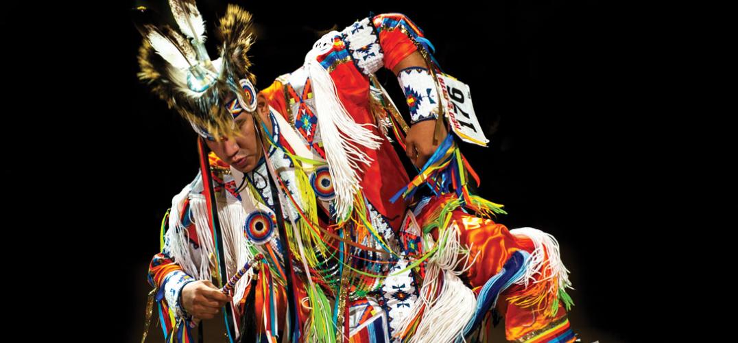 A grass dancer in an elaborately decorated outfit, captured mid-dance