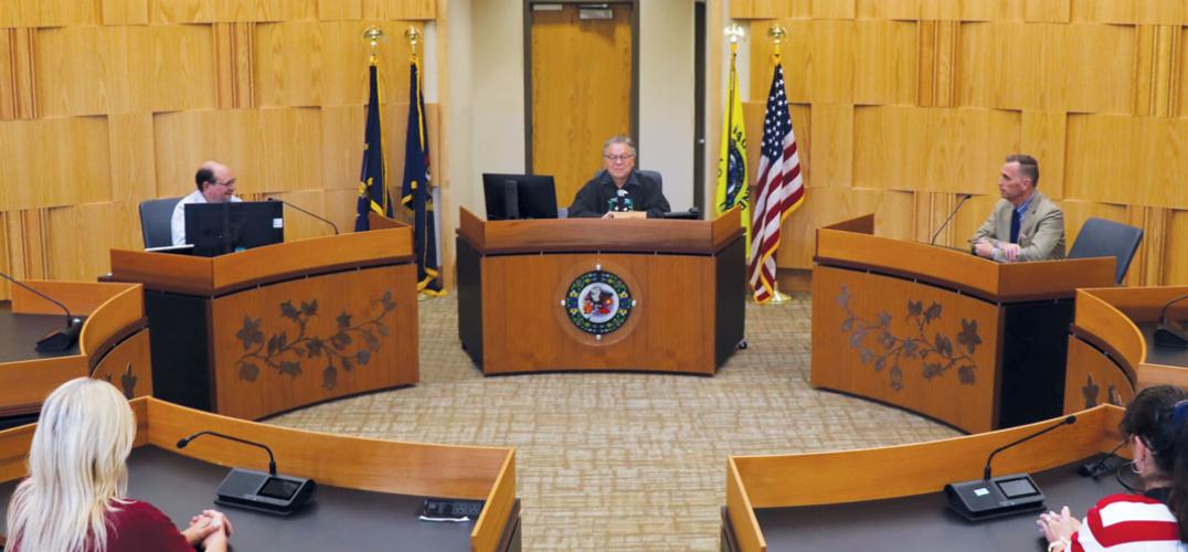 A courtroom with people, including a judge, sitting at tables arranged in a circle
