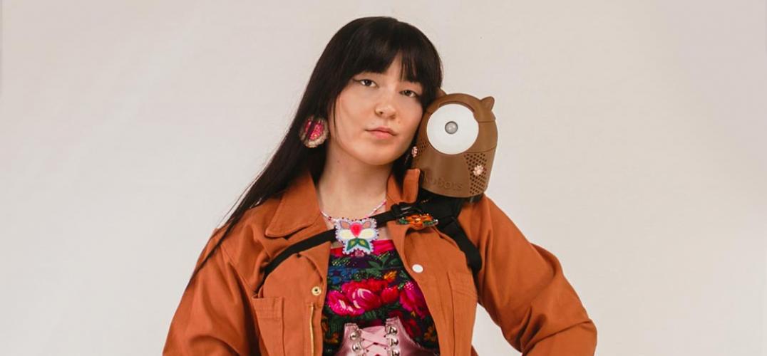 Inventor Danielle Boyer wears orange coveralls and holds a small brown robot on her shoulder.