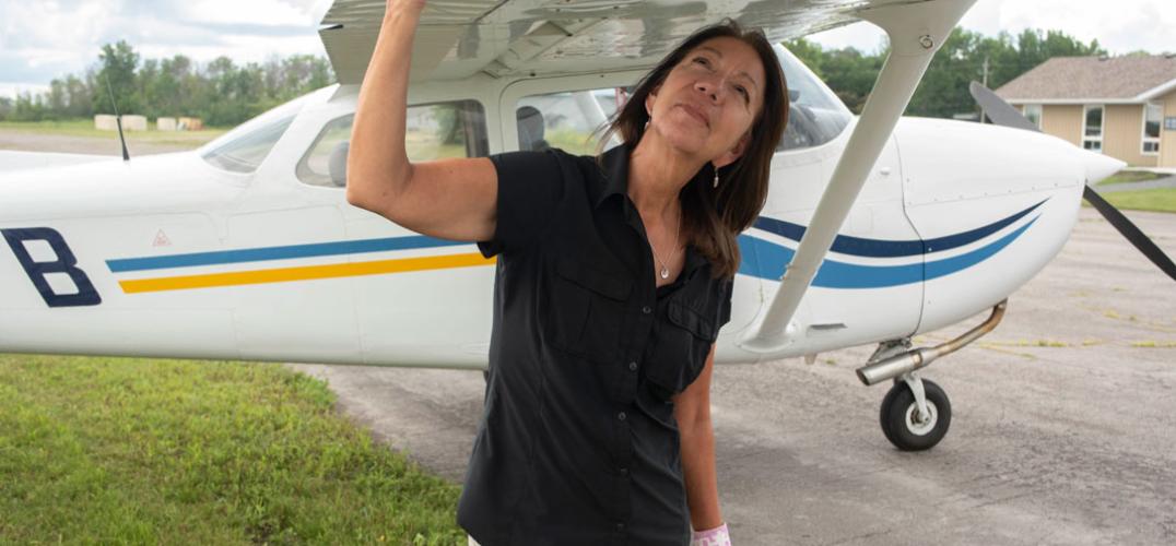Jo-Anne Tabobandung stands beneath and holds the wing of her airplane.