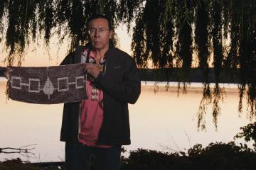 Sid Hill standing near Onondaga Lake, holding the Hiawatha Belt