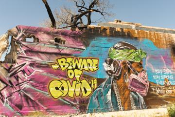 A mural depicts a man in traditional dress wearing a respirator and warns residents of COVID-19.