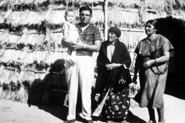 Walter Lamar as an infant is held by his father and is with his great-grandmother and grandmother in front of a traditional Wichita grass dwelling