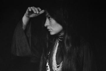 Zitkala-Ša, a Yankton Sioux woman, wearing traditional clothing and holding her hand to her forehead