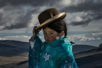 Young Bolivian girl in traditional cholita attire tips her bowler hat