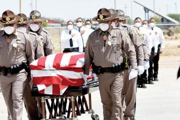 Six officers, masked and in uniform, pull a wooden casket while others around them salute or cover their hearts
