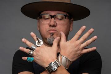 Artist Erik Lee holding up his hands, showing silver rings and bracelets he created