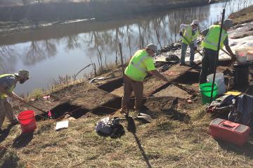 Archaeology crew members work along a riverbed in Iowa