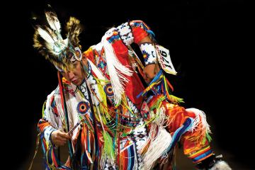 A grass dancer in an elaborately decorated outfit, captured mid-dance
