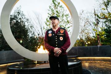 A man in uniform stands in front of a tall metal circle with a lit flame at its base