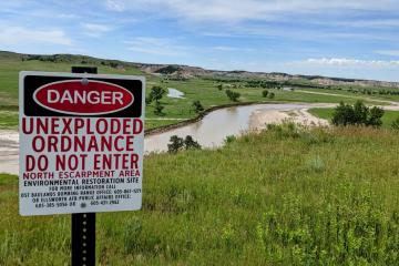 A posted sign warning of unexploded ordnance in front of a landscape