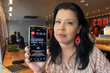 Journalist Francine Compton holds up a phone with a message that her access to CNN news feed is blocked in a cafe