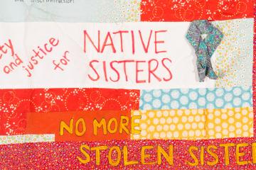 A closeup of a quilt piece with text, including the words "No More Stolen Sisters" 
