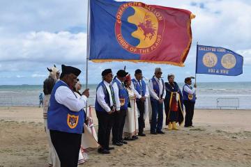 Descendants of code talkersstand in a line on a beach, holding several large flags