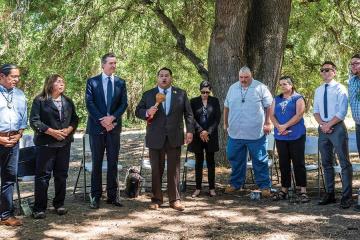 A group of Indigenous Californians standing in a circle with the California governor under trees