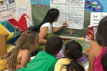 Students watch their teacher write about Indigenous foods on a board
