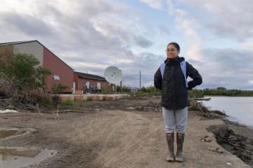Student Madison Andrew standing near a school house on the shore of the Kuskowim River.
