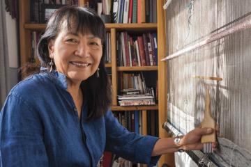 Artist DY Begay smiling while working on a large weaving in her studio.