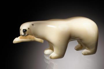 An ivory figurine of a polar bear holding a fish in its mouth on a black background.
