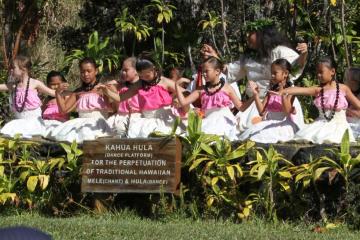 Group of children in white and pink dresses performing hula on stage