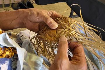 Hands weaving leaves into crown of hat 