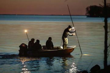 Group of Indigenous fishers spearfishing from a boat at dusk