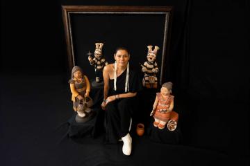 Kathleen Wall posing with four clay sculptures on dark background