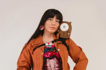 Inventor Danielle Boyer wears orange coveralls and holds a small brown robot on her shoulder.