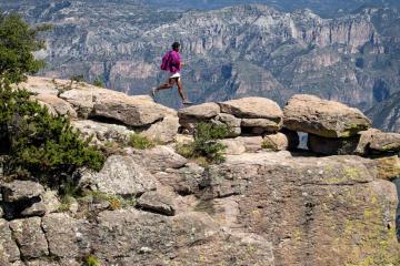 Person in traditional clothing and sandals running on top of rocky desert cliff.