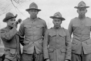 Four soldiers, one playing a bugle, stand in line