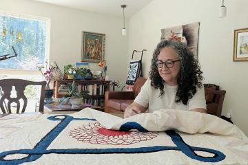 Emma Alcazar sews a red, white, and blue quilt at a table in her sunny, art-filled home.