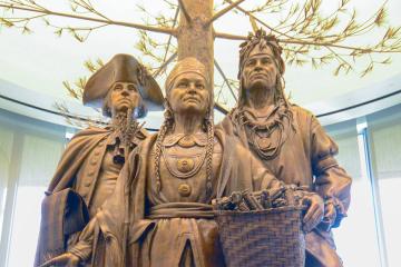 A bronze sculpture depicting Oneida Chief Shenendoah, General George Washington, and Polly Cooper standing under a towering tree amongst fruits and animals.