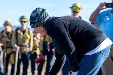 Yana Ross lights a prescribed fire with a red tank in a field of dry grass.